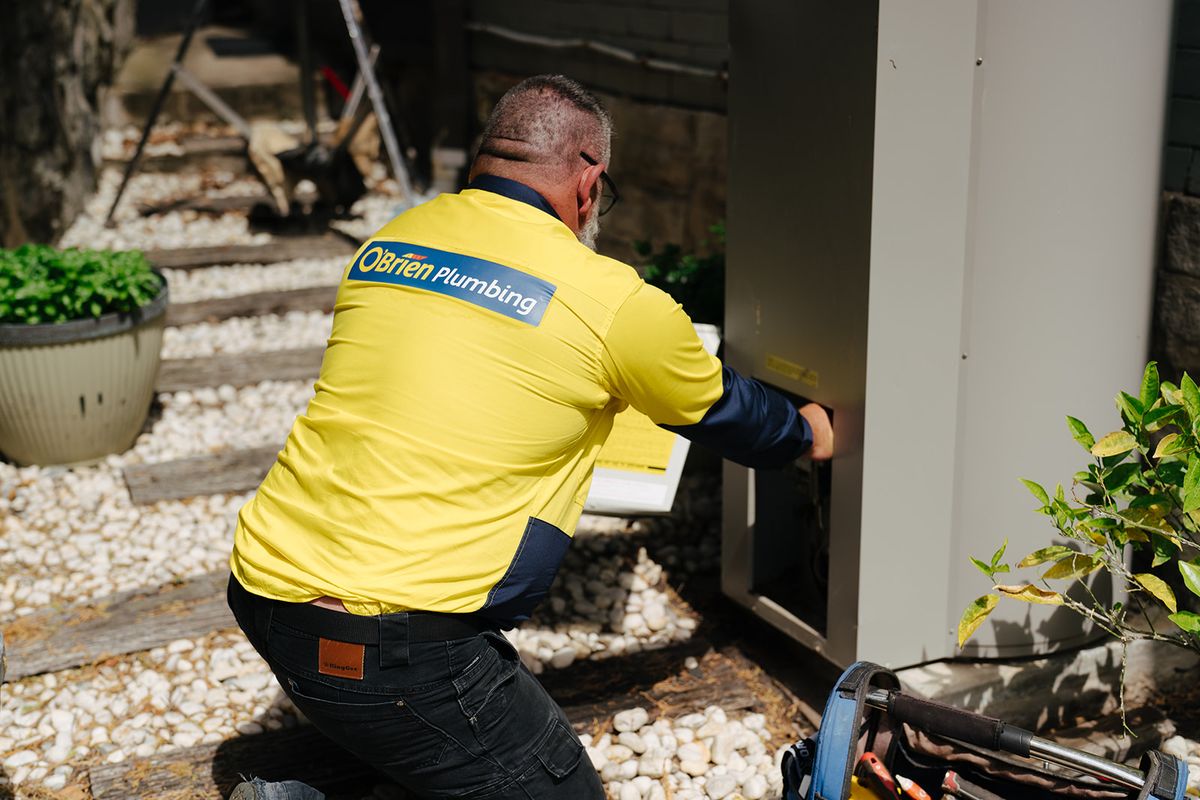 An O’Brien plumber working on an externally mounted hot water system