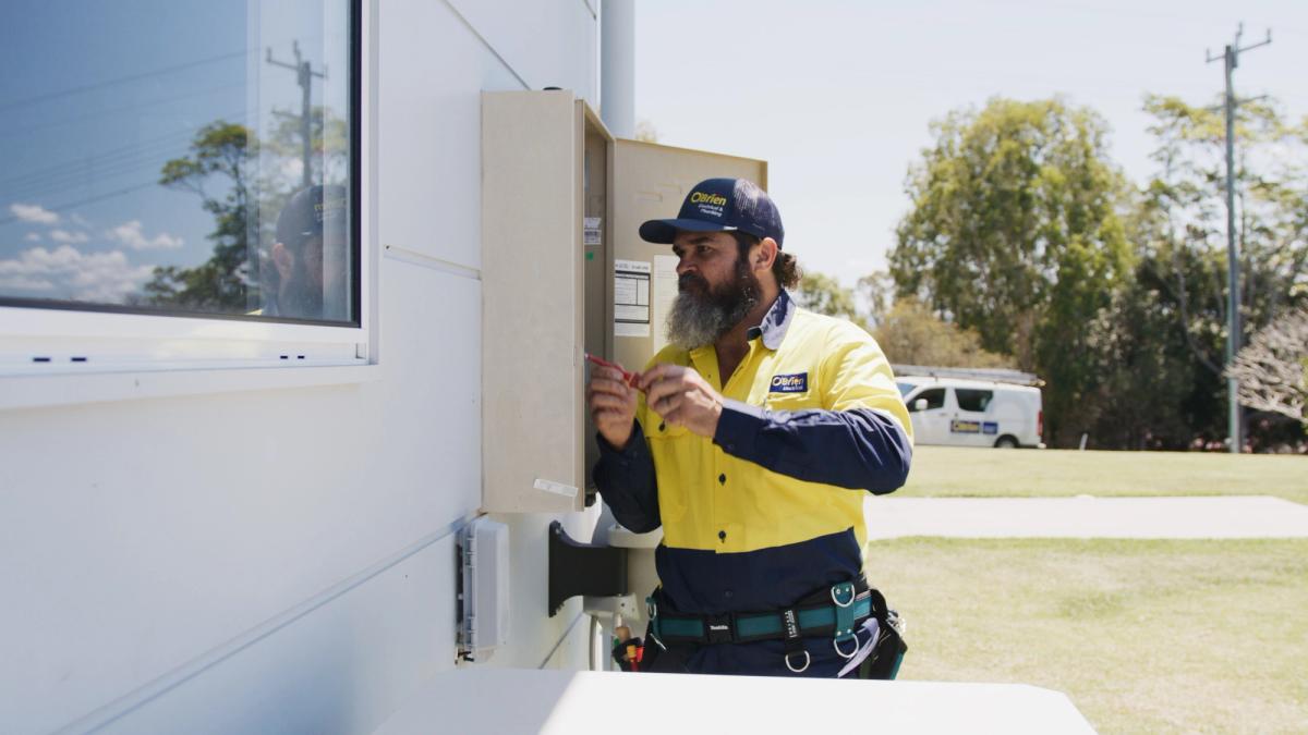 An O’Brien electrician working at an outdoor meter box with a work van parked behind