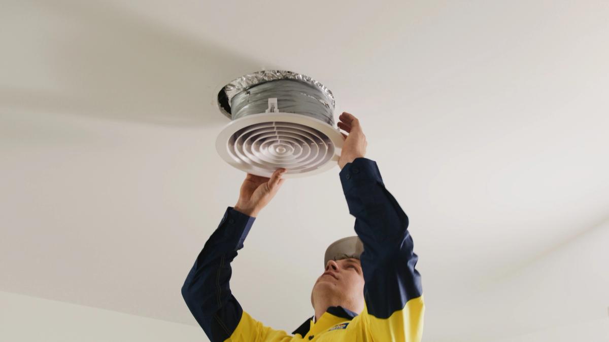 A technician fitting a round ceiling air conditioning vent