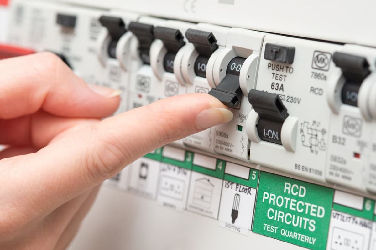 A finger switching an RCD safety switch on a labelled switchboard