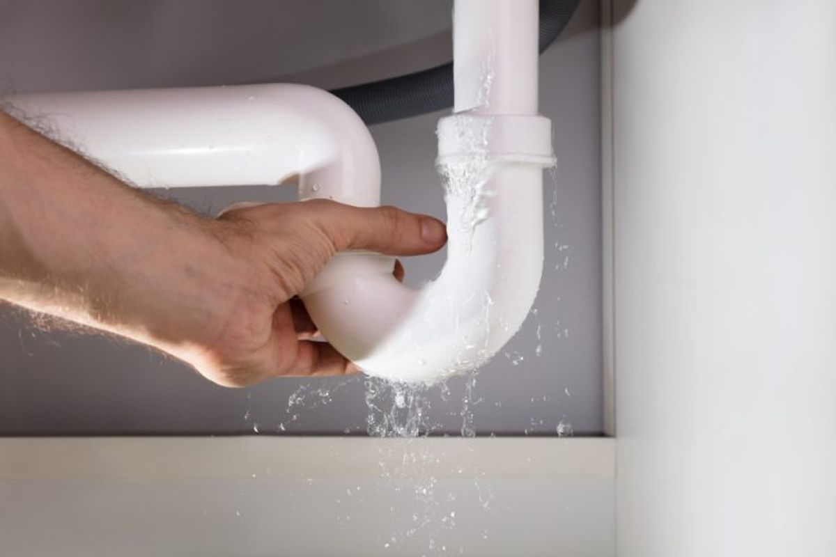 A hand holding a leaking waste pipe under a basin as water sprays out