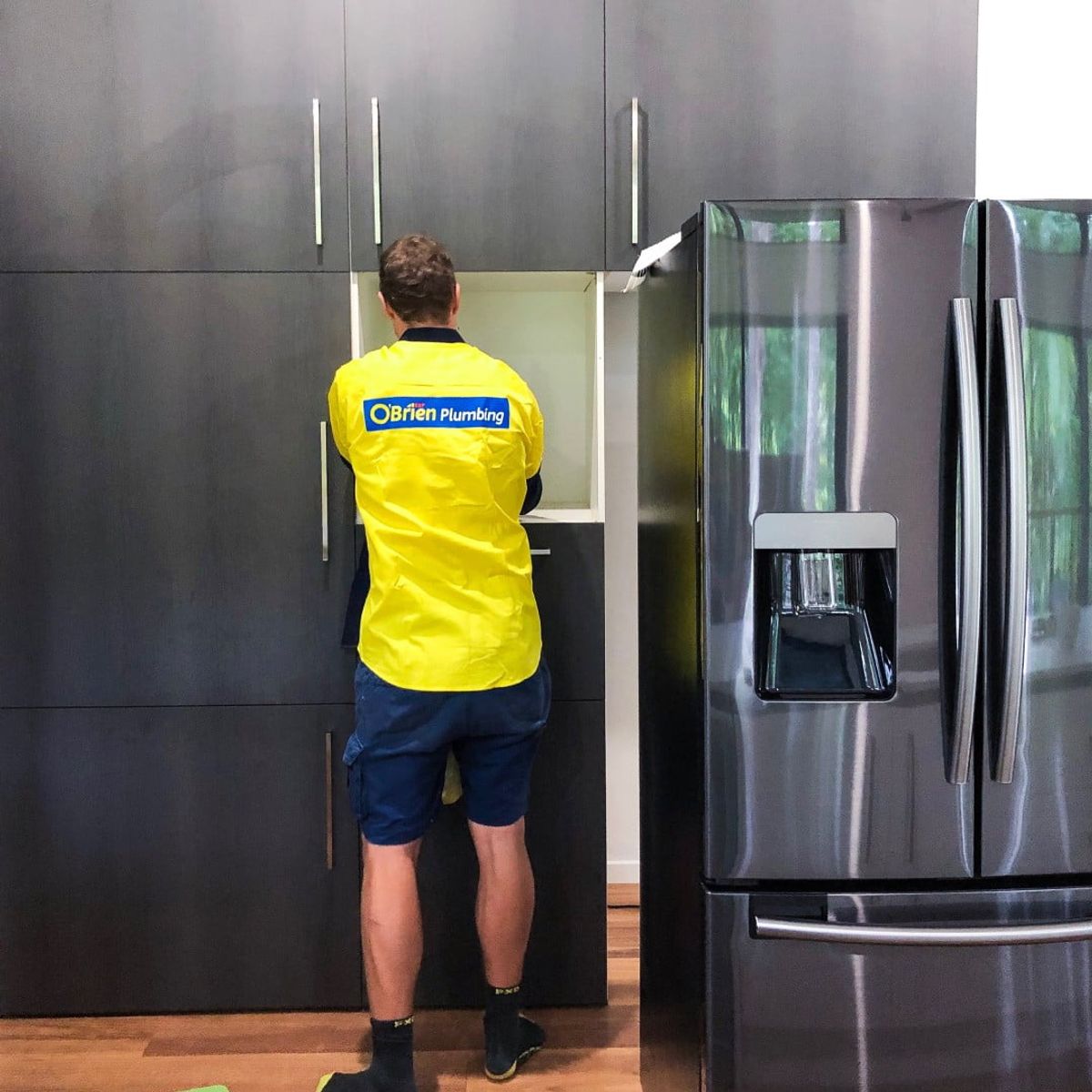 An O’Brien plumber connecting the water line to a fridge