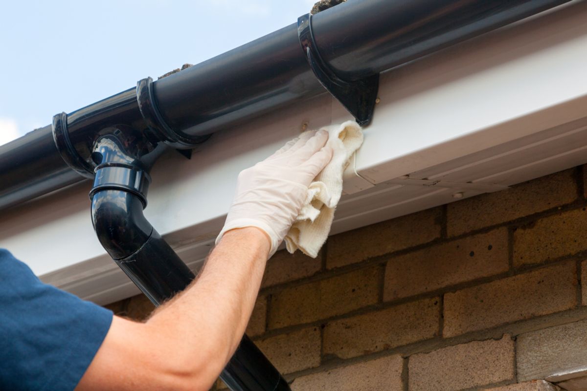 A gloved hand wiping the edge of guttering beside a downpipe