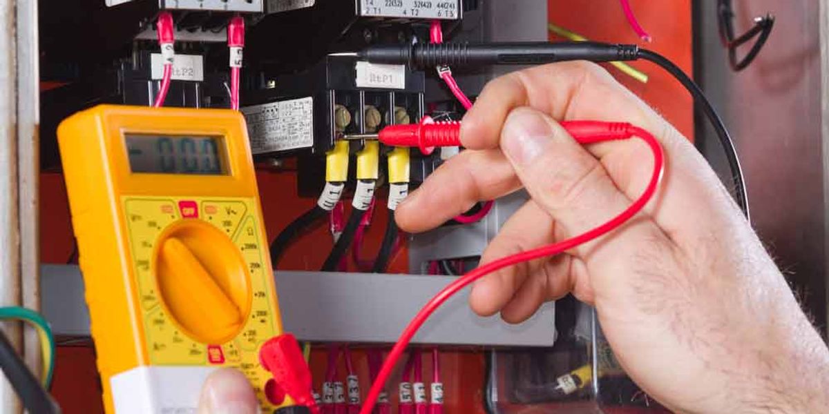 Hands probing an electrical control panel with a multimeter