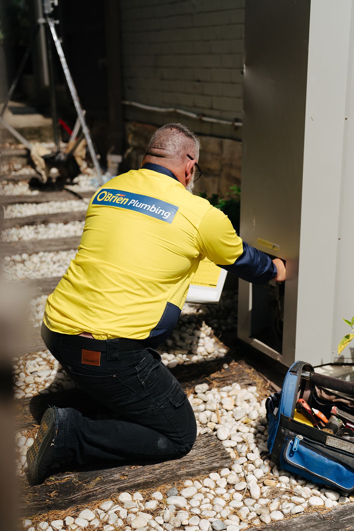 An O’Brien plumber kneeling at an externally mounted hot water system