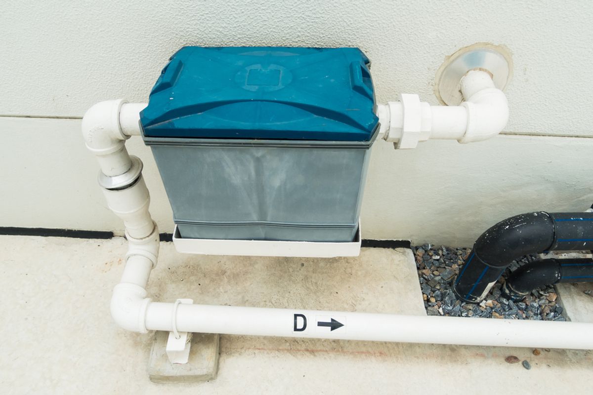 A grease trap connected to white pipework beside a building