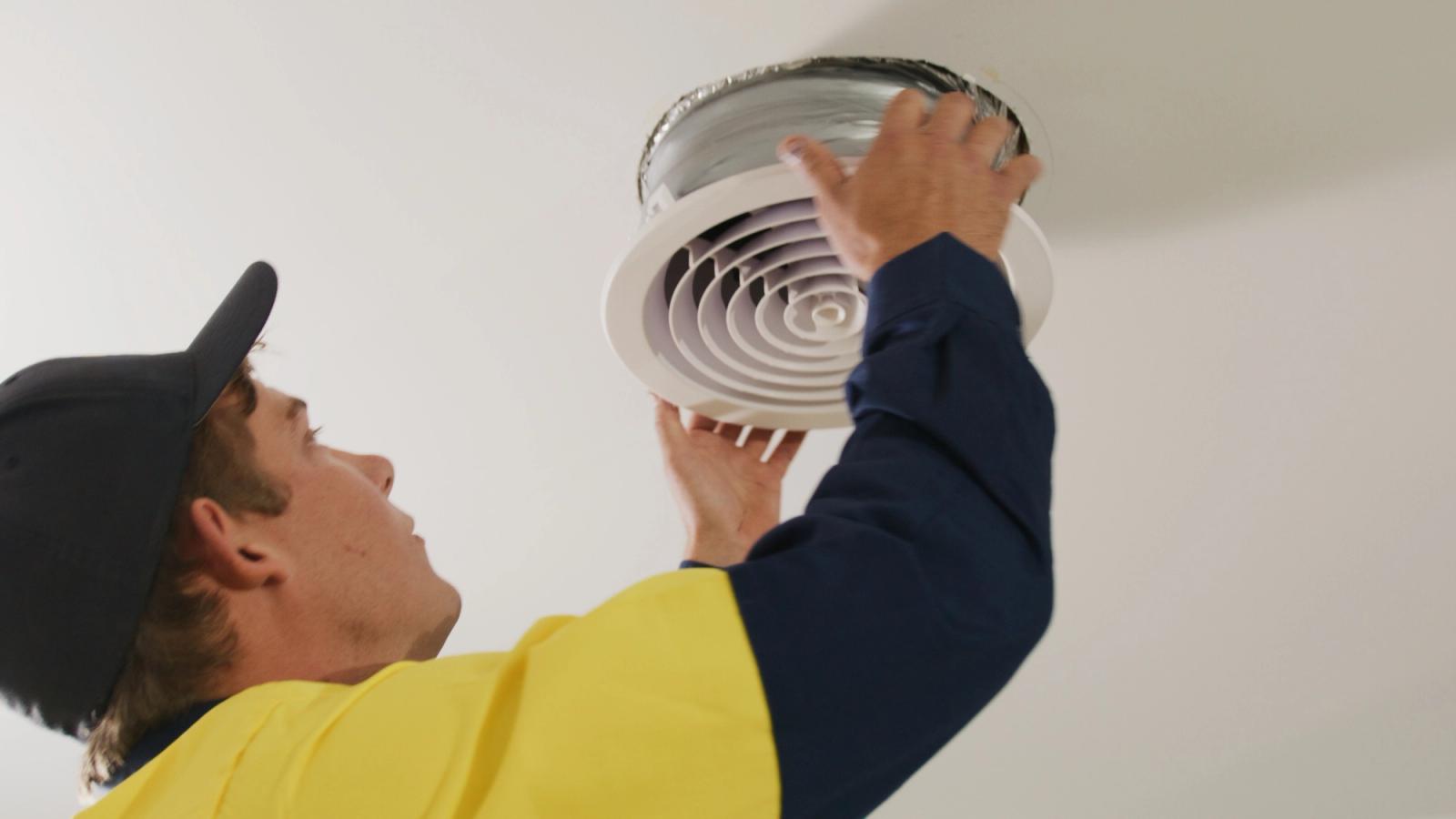 Two technicians in hi-vis fitting a round ceiling vent