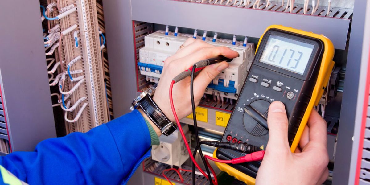 Hands testing circuit breakers in an electrical cabinet with a multimeter