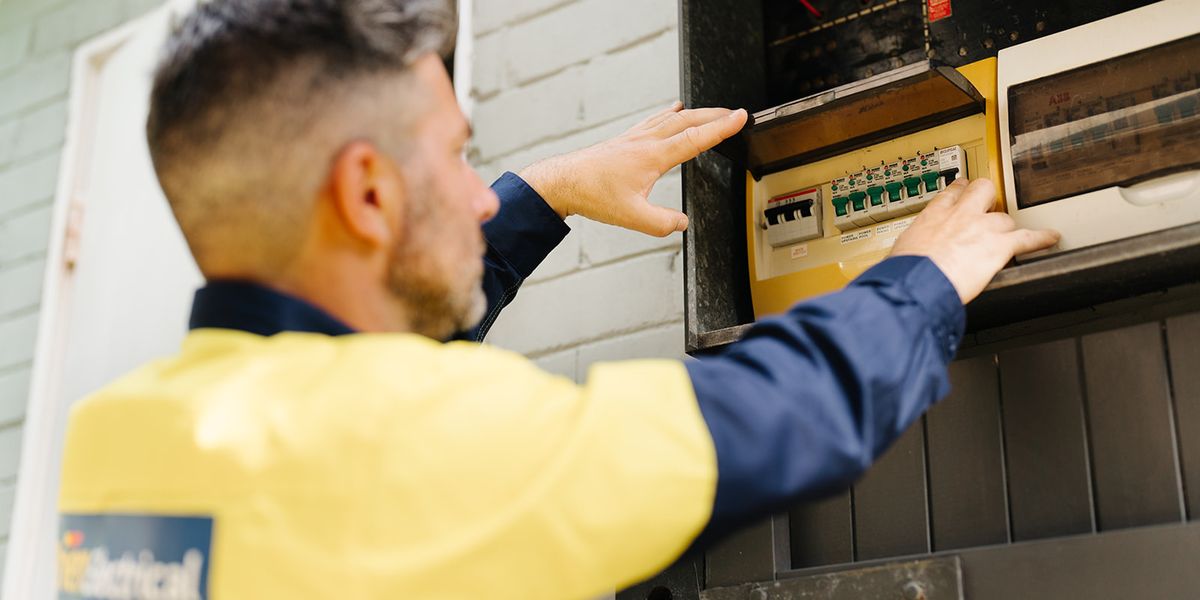 An electrician in hi-vis opening an outdoor meter box on a brick wall