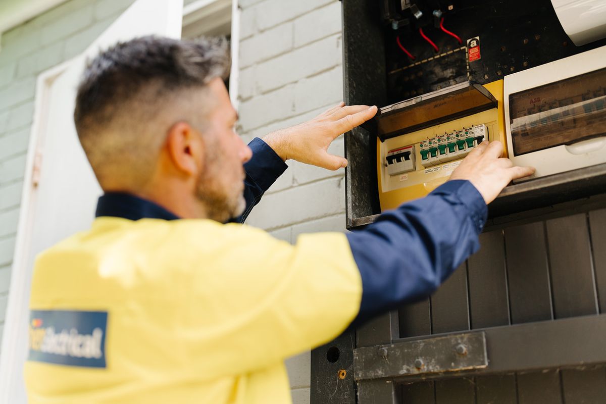 An electrician in hi-vis opening an outdoor meter box on a brick wall