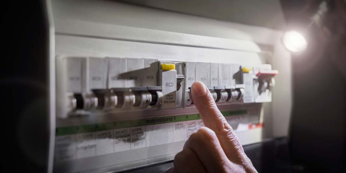 A hand checking a switchboard by torchlight during a power outage