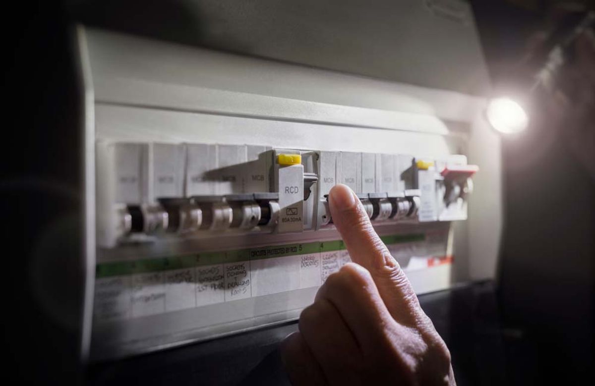 A hand checking a switchboard by torchlight during a power outage