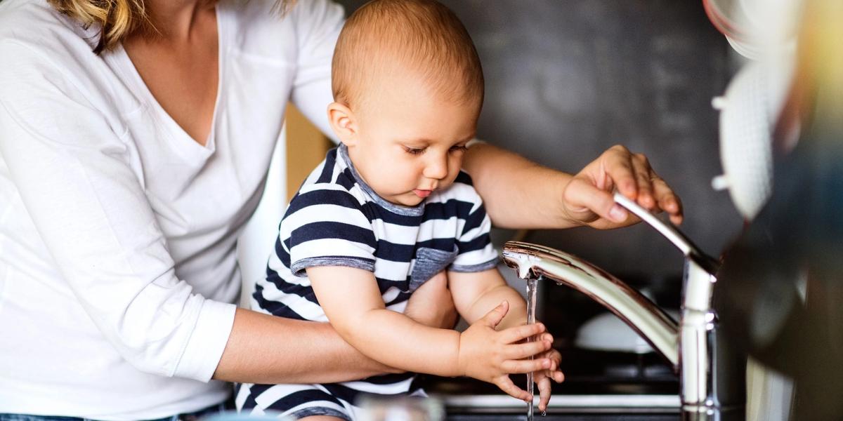 A parent holding a baby beside a running kitchen tap