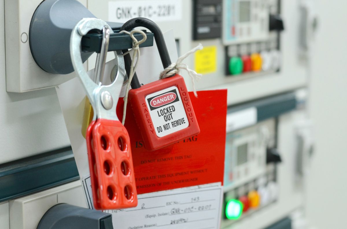 A red lockout tag and hasp fitted to an industrial control panel