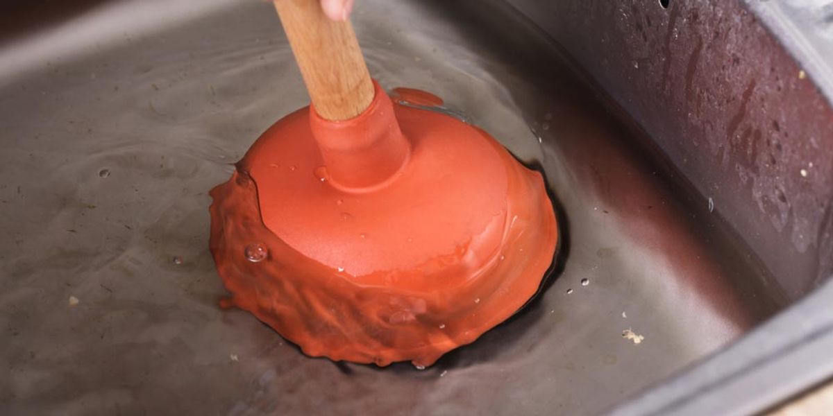 A plunger being used in a stainless steel kitchen sink