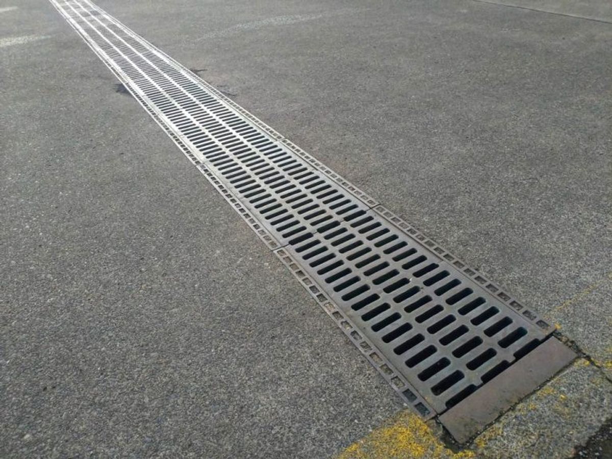 A metal grate trench drain running across a concrete driveway