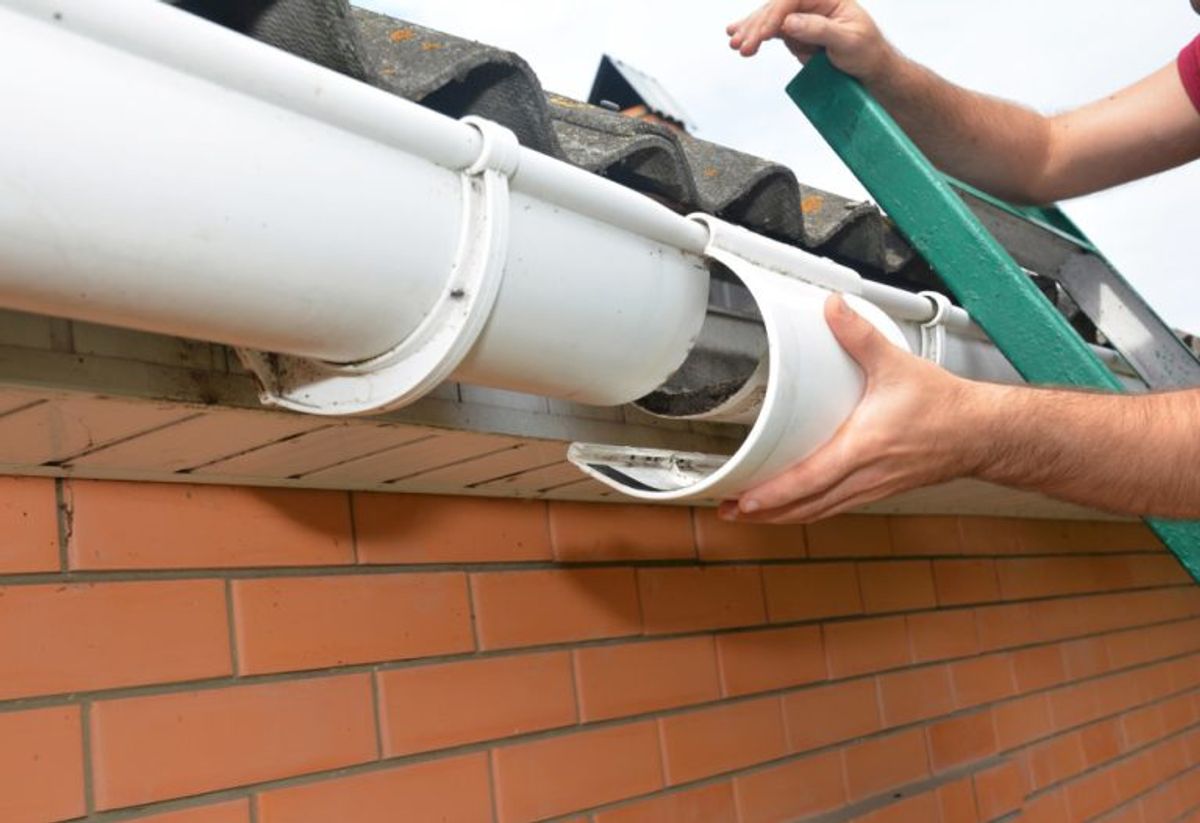 Hands fitting a length of white guttering along the edge of a roof