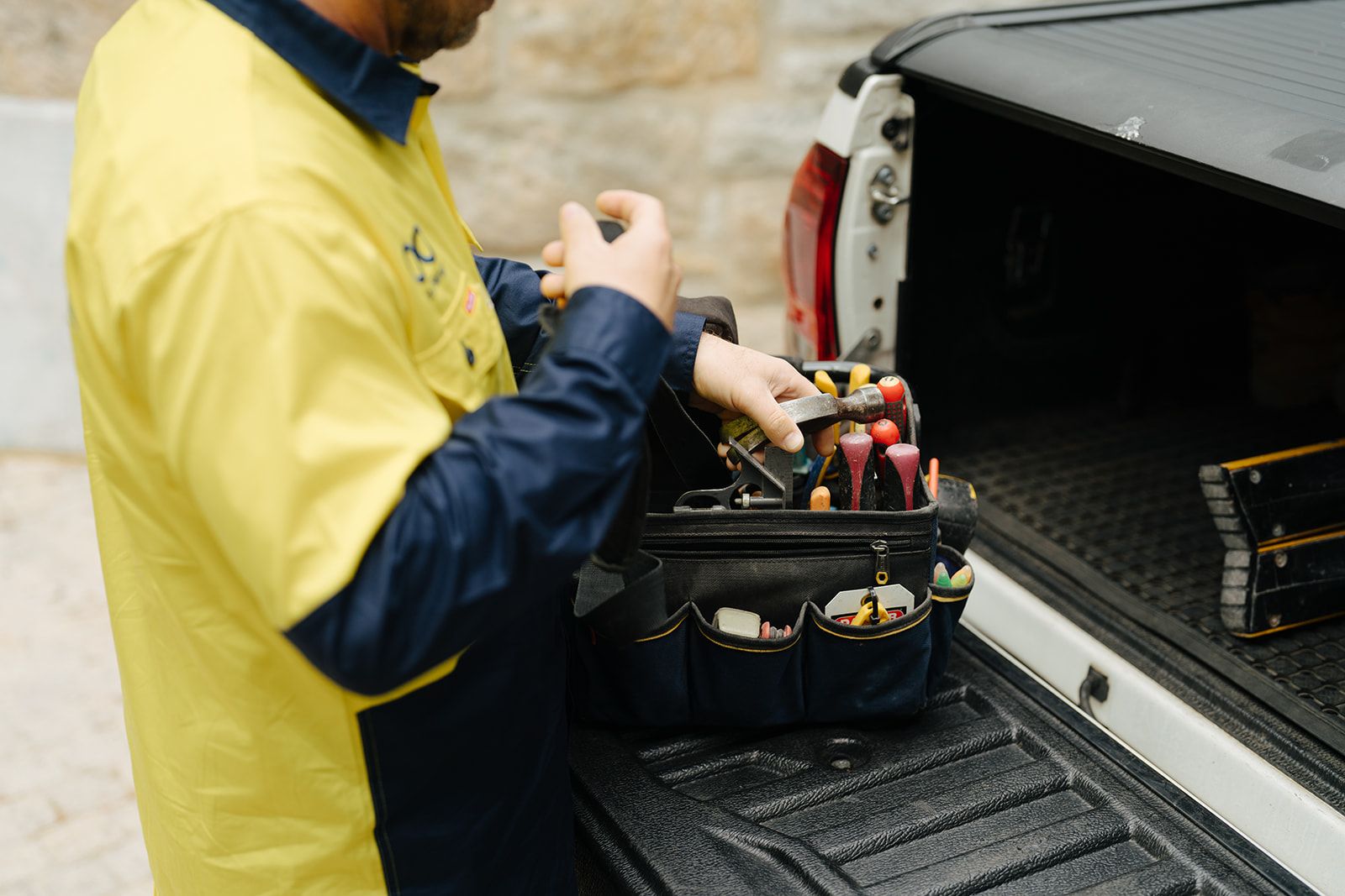 A technician taking tools from a bag in the tray of a work ute