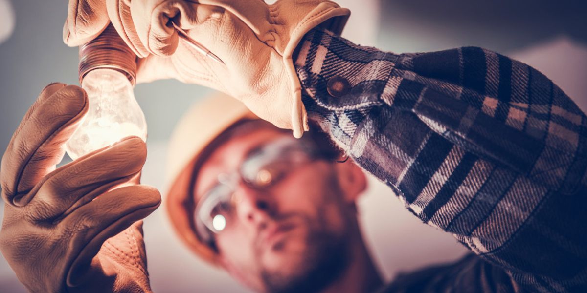 A worker in a hard hat and gloves fitting a light globe