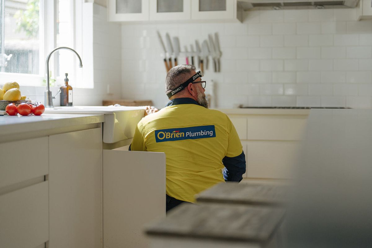 An O’Brien plumber working under the sink of a white kitchen