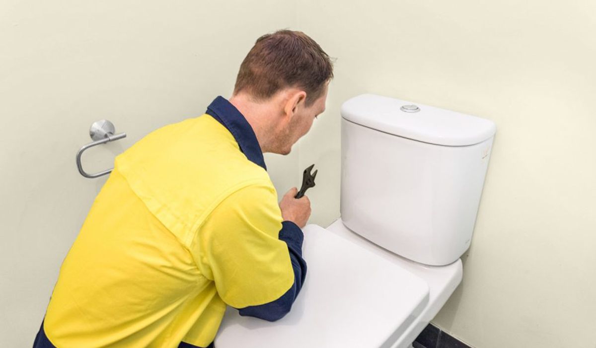 A plumber working on a toilet cistern with a spanner