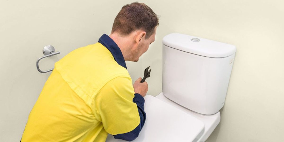 A plumber working on a toilet cistern with a spanner