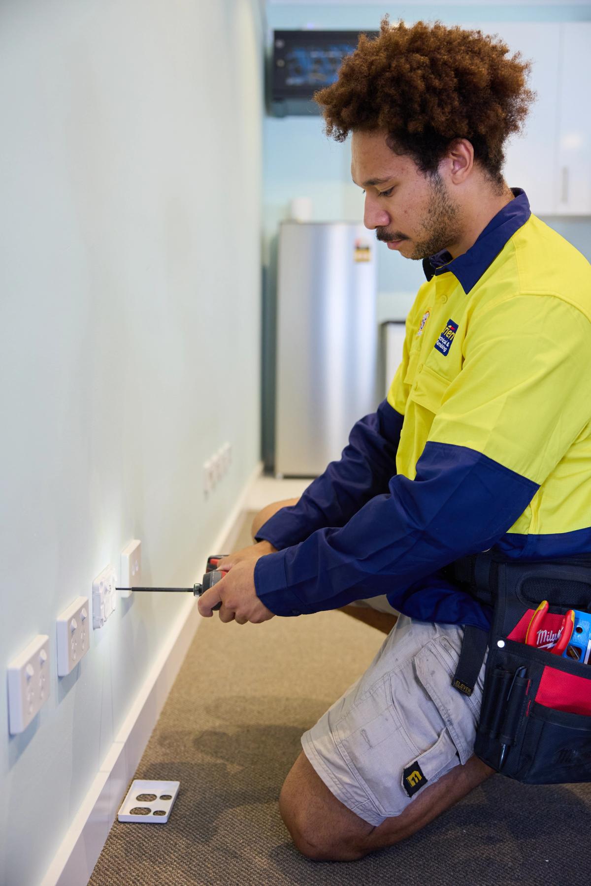 An O’Brien electrician kneeling to fit a power point in a hallway