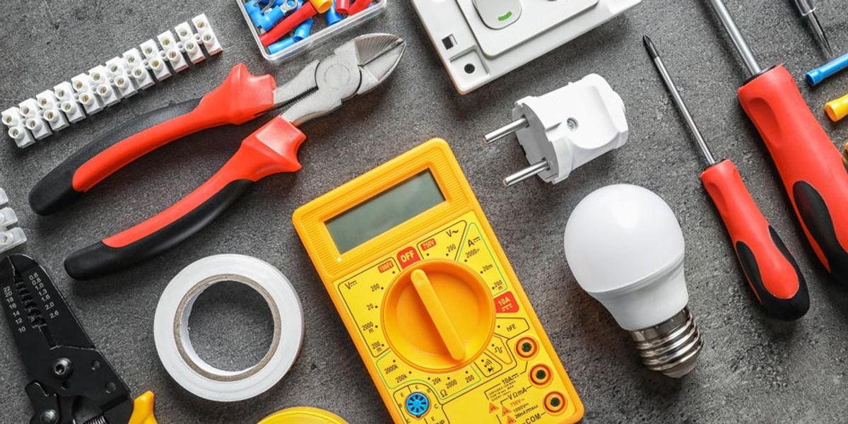 Electrical tools, a multimeter and a light globe laid out on a bench