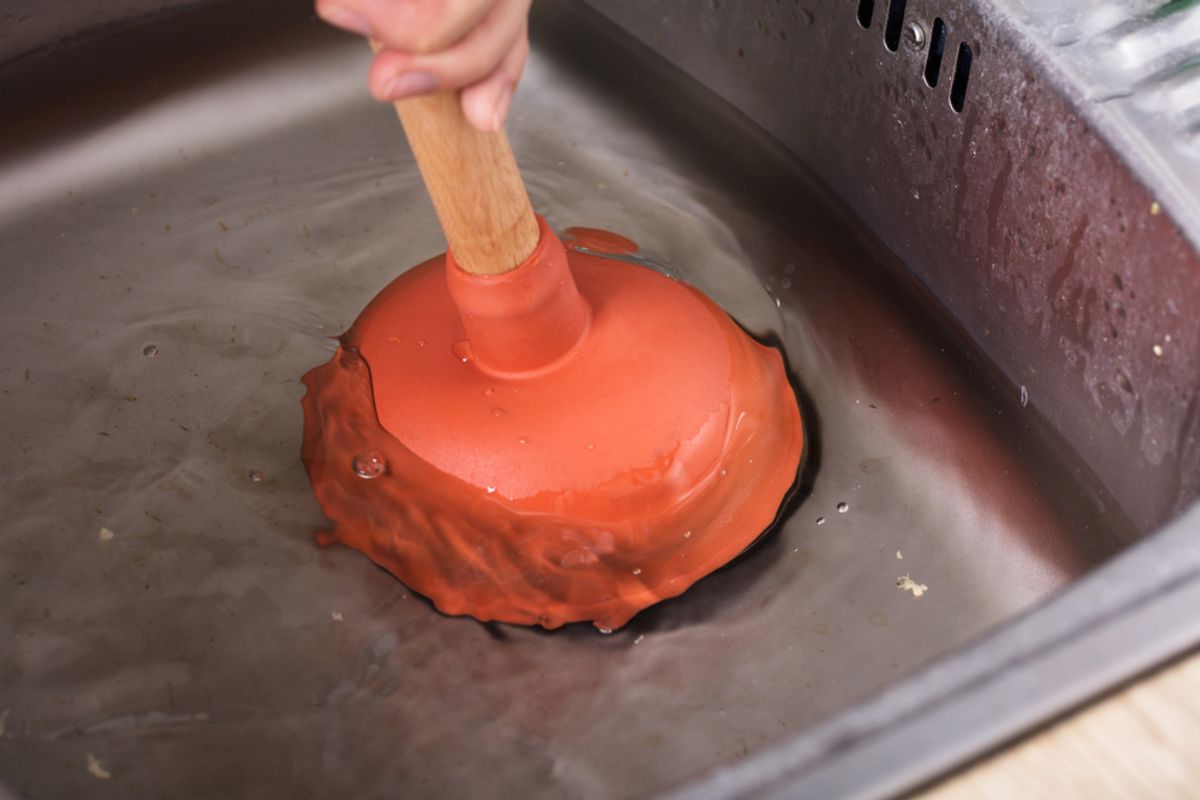 A plunger being used in a stainless steel kitchen sink