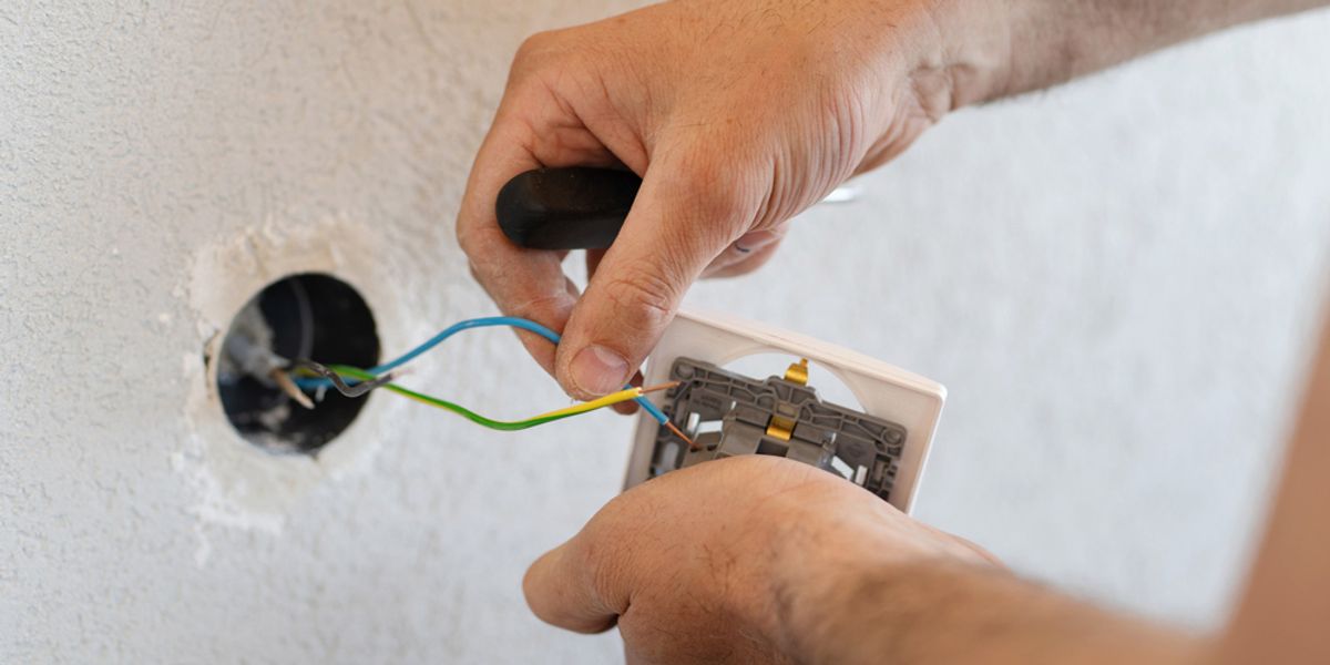 Hands wiring a power outlet into a wall cavity