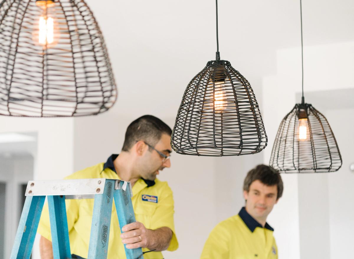 Two O’Brien electricians in hi-vis fitting woven pendant lights, one on a step ladder