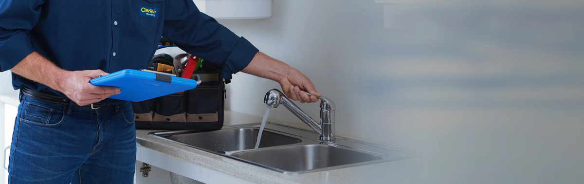 A plumber in an O’Brien shirt running the tap at a stainless steel double sink