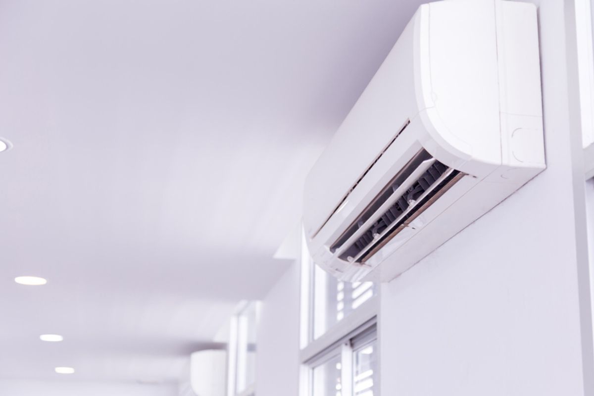 A wall-mounted split system air conditioner high on the wall of a bright white room