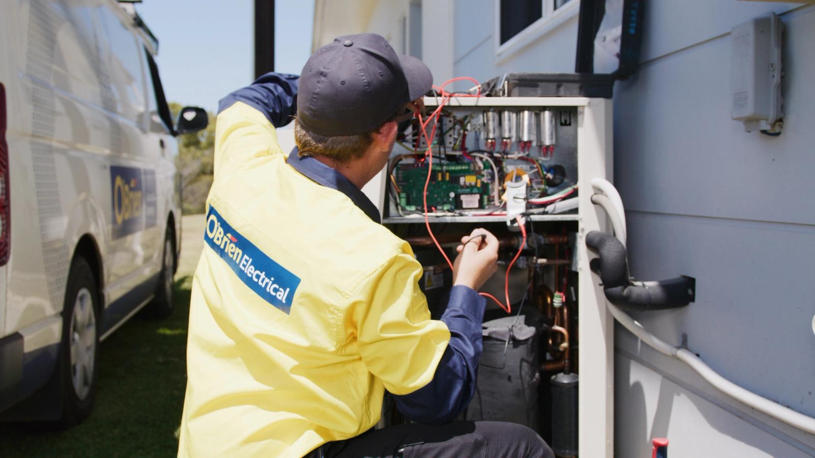 An O’Brien electrician working at the open control panel of an outdoor unit beside a van
