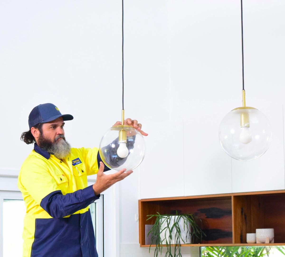 An O’Brien electrician steadying a clear glass globe pendant light in a kitchen