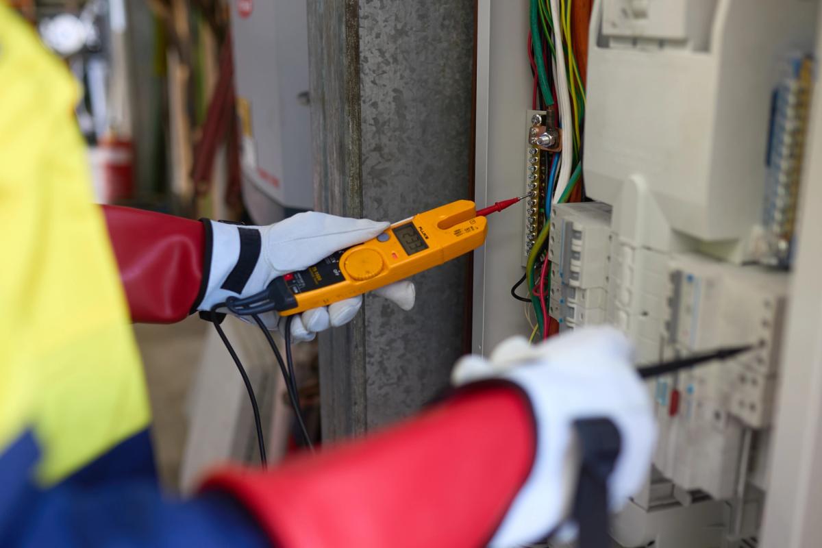 Gloved hands testing a switchboard with a two-pole voltage tester