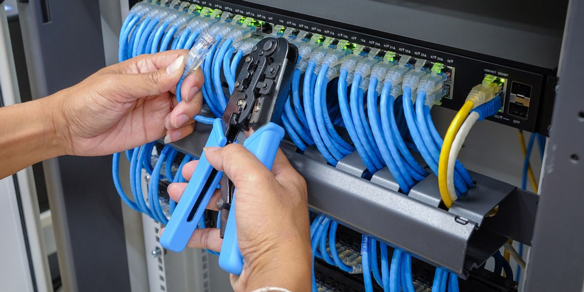 Hands crimping blue network cables at a patch panel in a communications rack