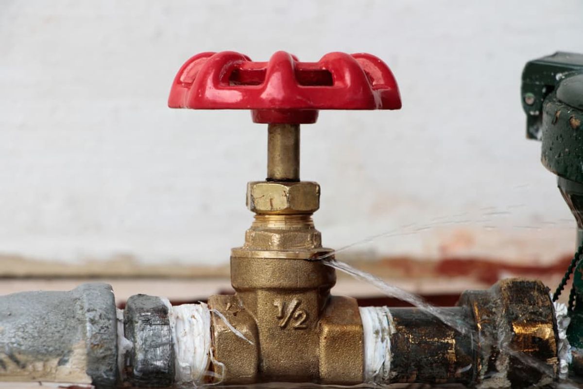 Water spraying from a brass isolation valve on corroded pipework