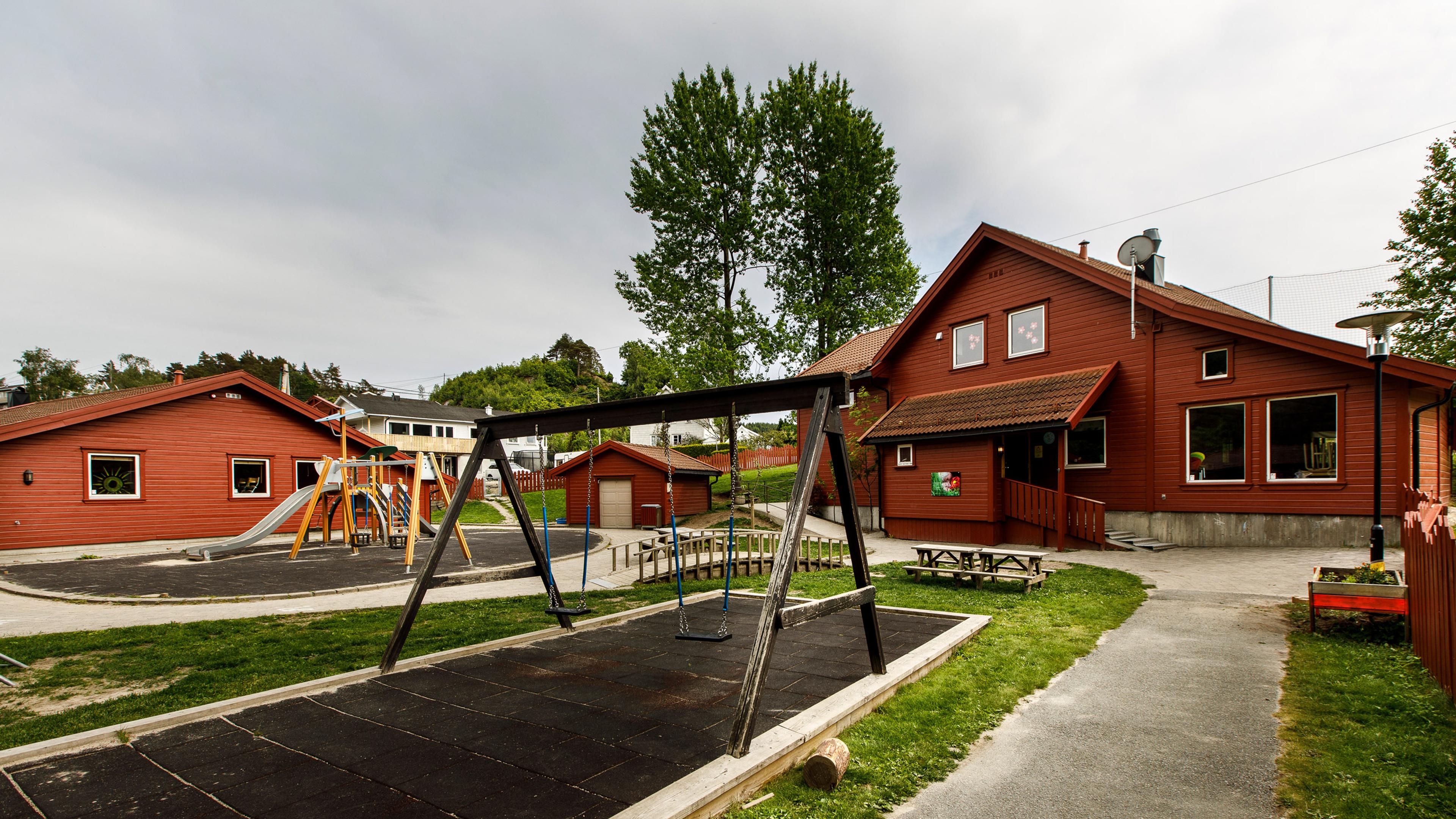 Uteområdet til Espira Holum barnehage i Holum Mandal – rødt bygg med lekeplass rett utenfor