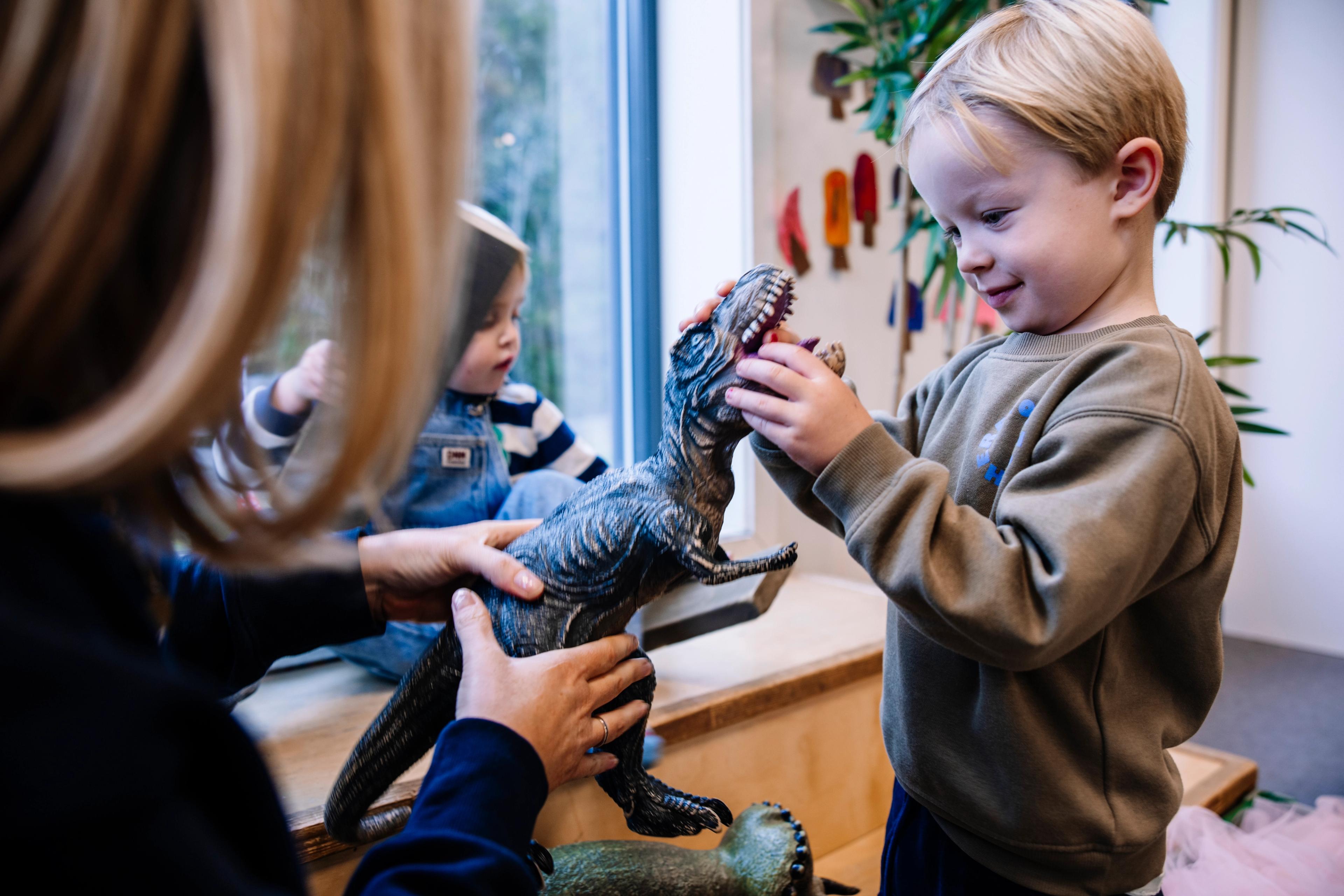 Voksen som leker med dinosaur sammen med barn - Espira barnehage