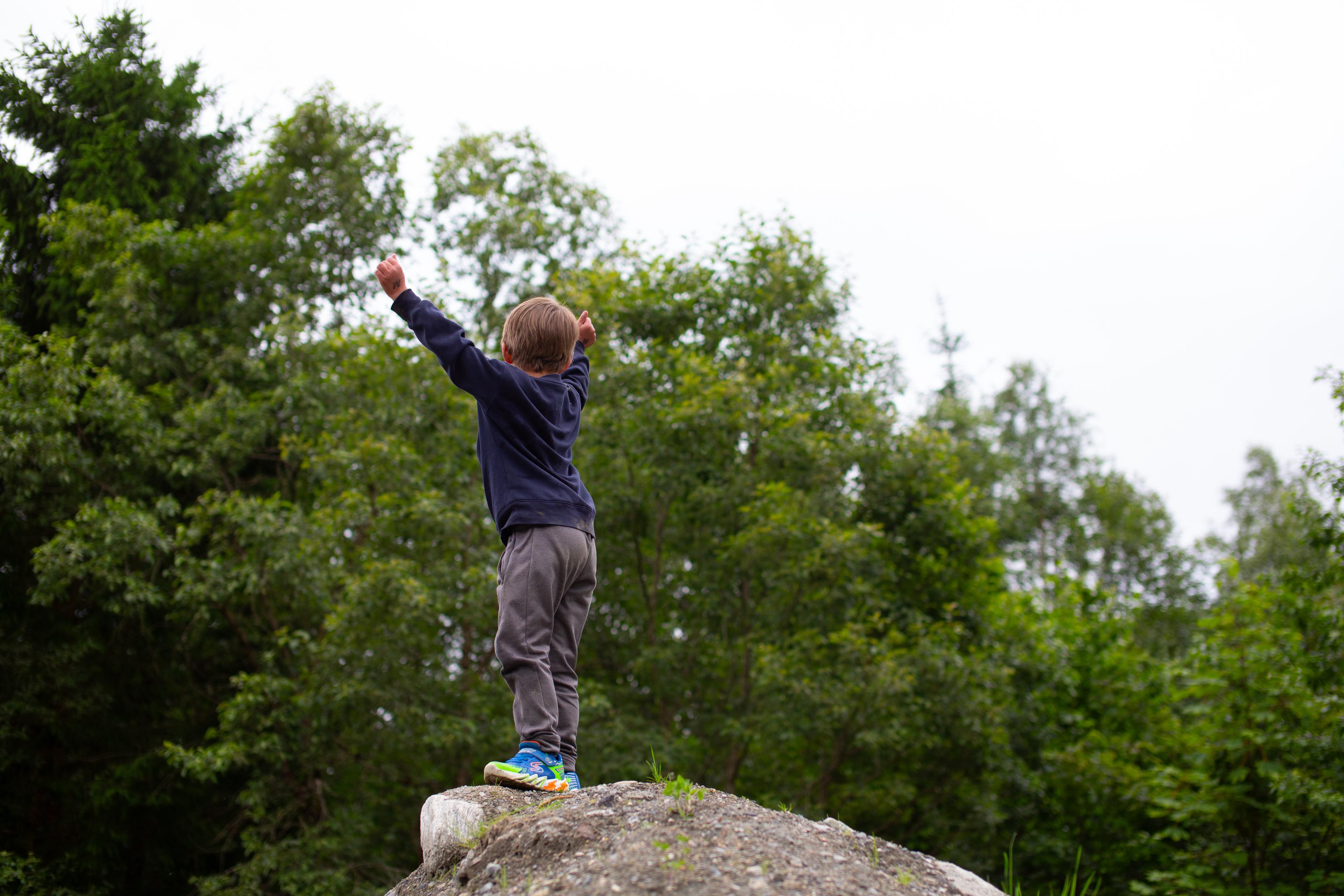 a young boy is standing on top of a rock with his arms in the air .