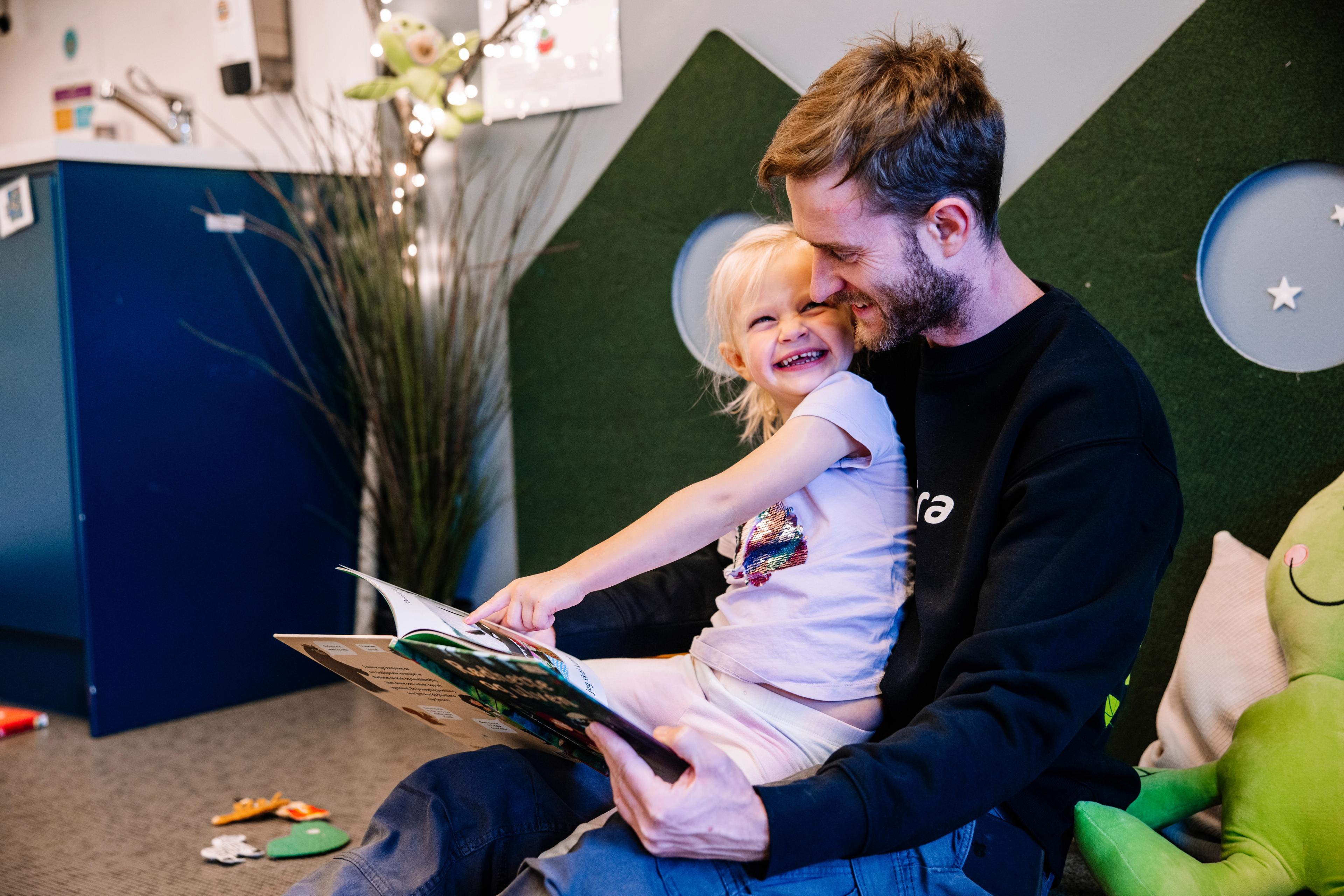 Mann og barn som har det gøy med å lese bok sammen - Espira barnehage