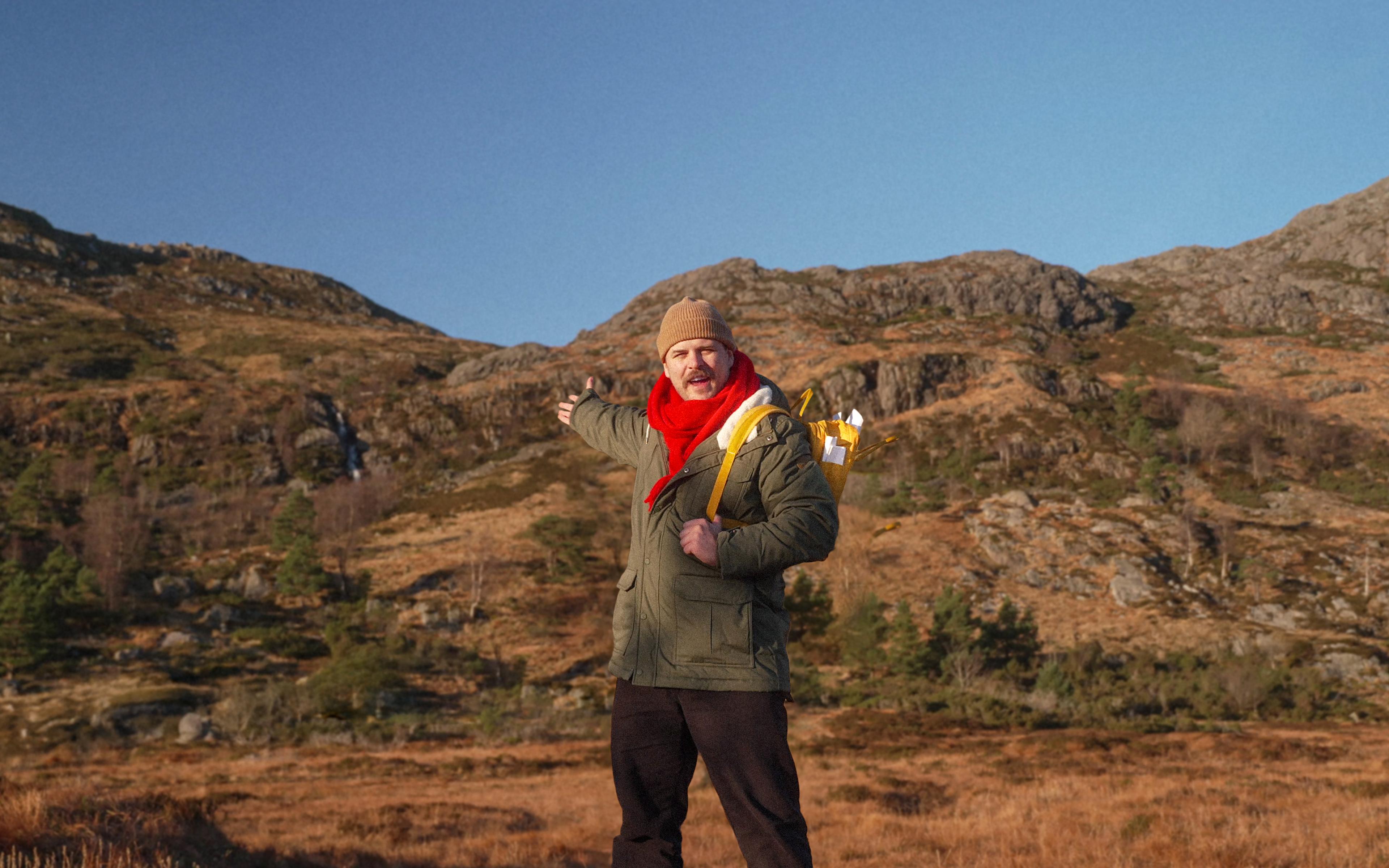 a man is standing in a field with his arms outstretched in front of a mountain .