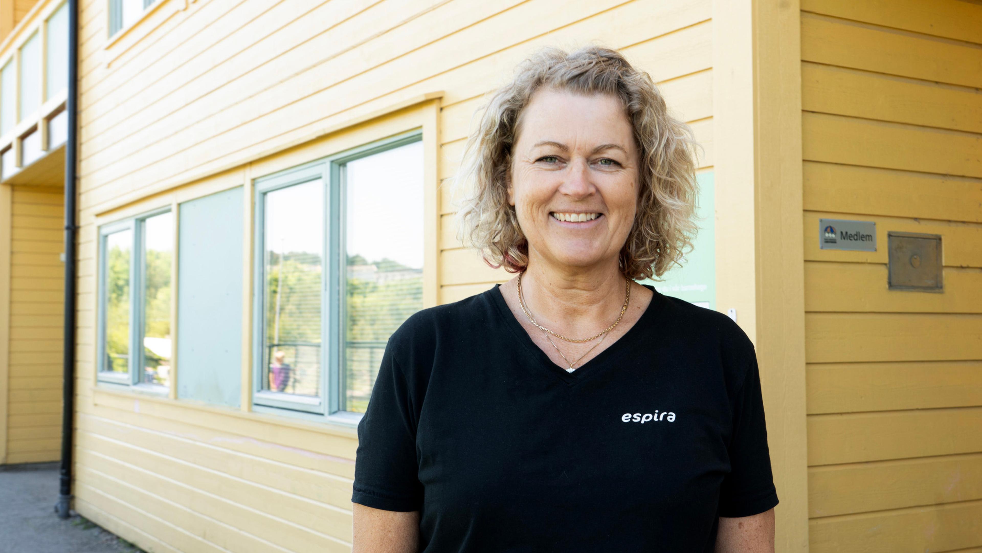 Portrett av Anita som står foran et trebygg.