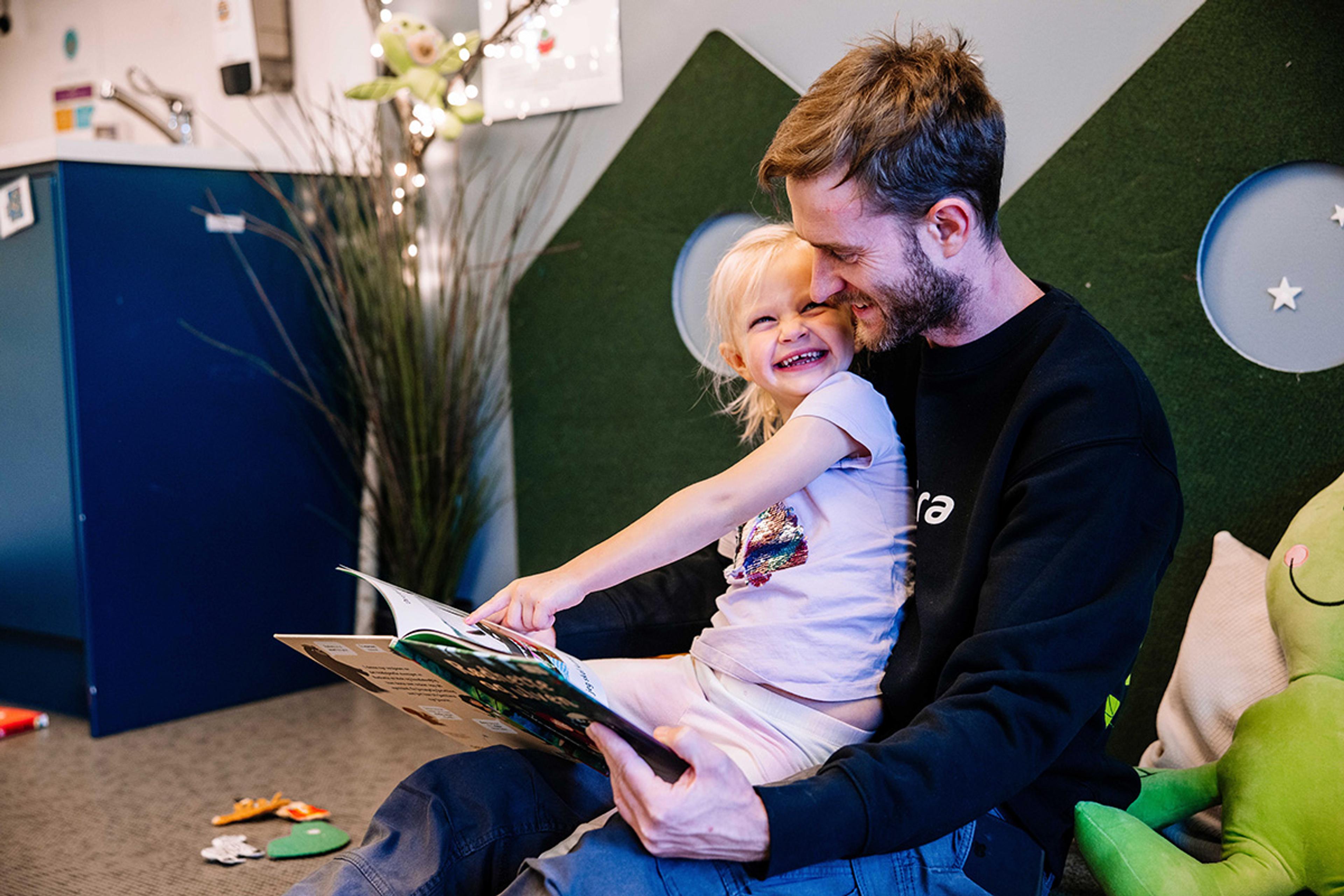 Mann leser for jente på gulvet.