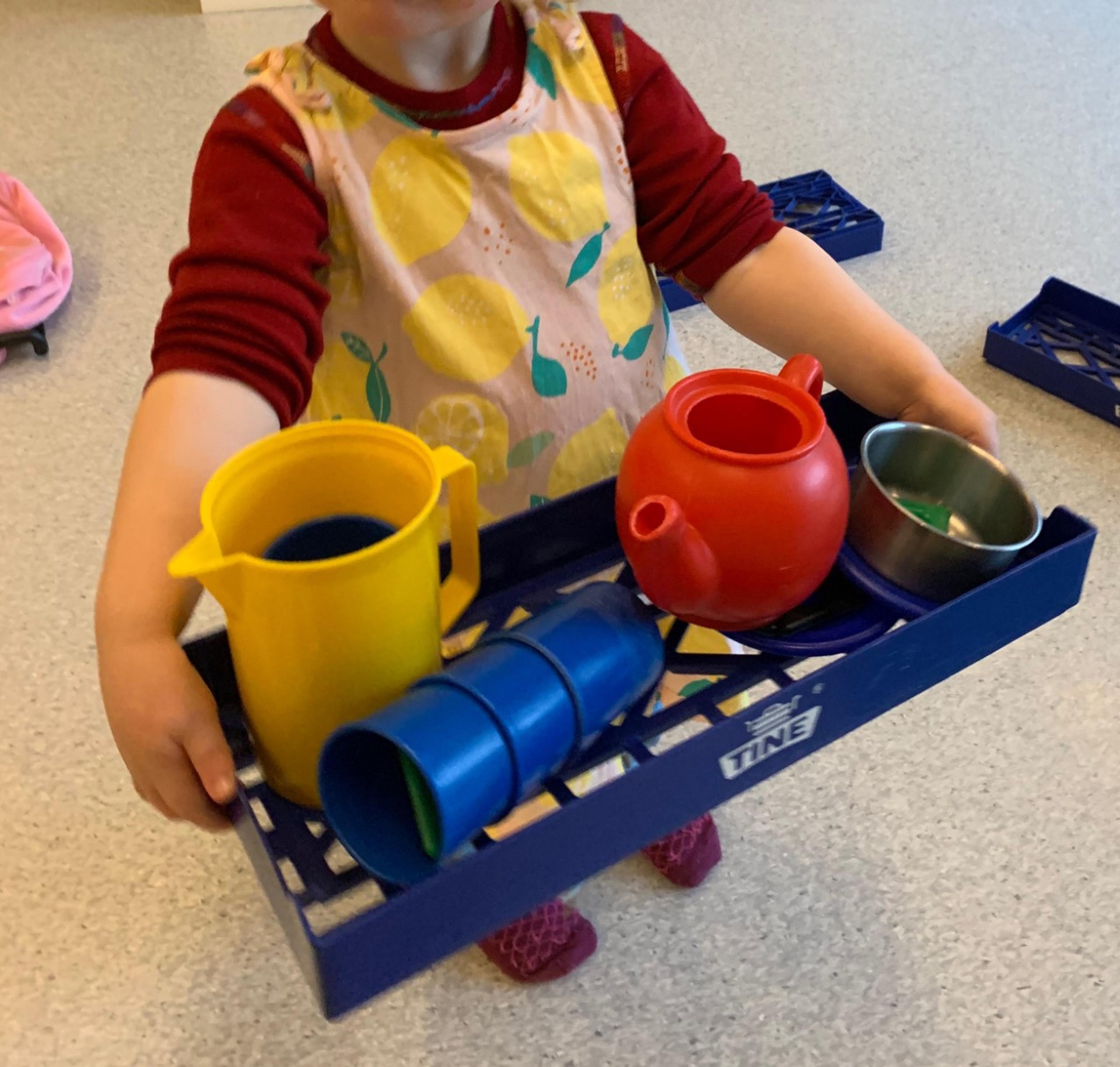 a little girl is holding a tray with a tea set on it .