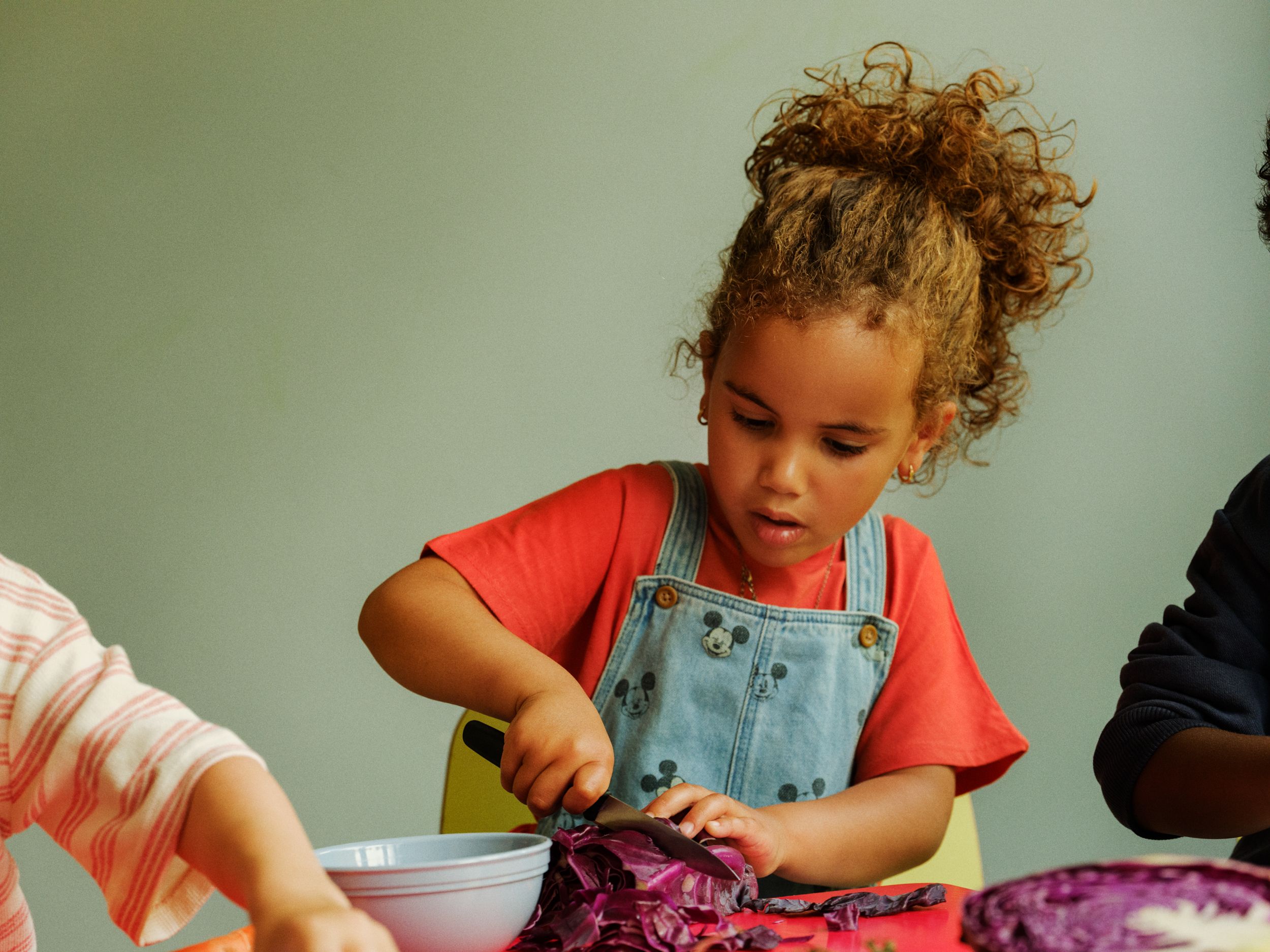 a little girl is cutting a red cabbage into a bowl .