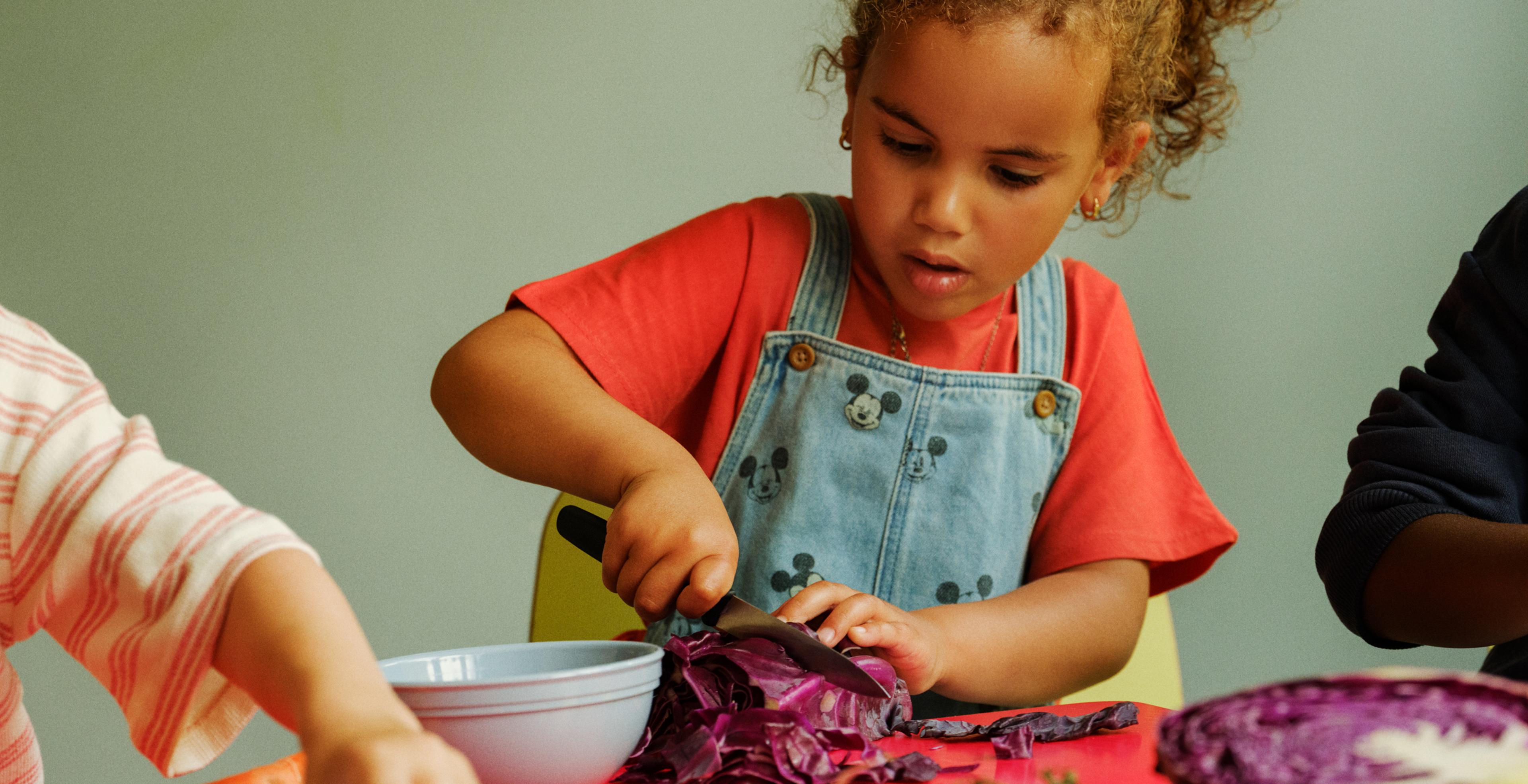 a little girl is cutting a red cabbage into a bowl .