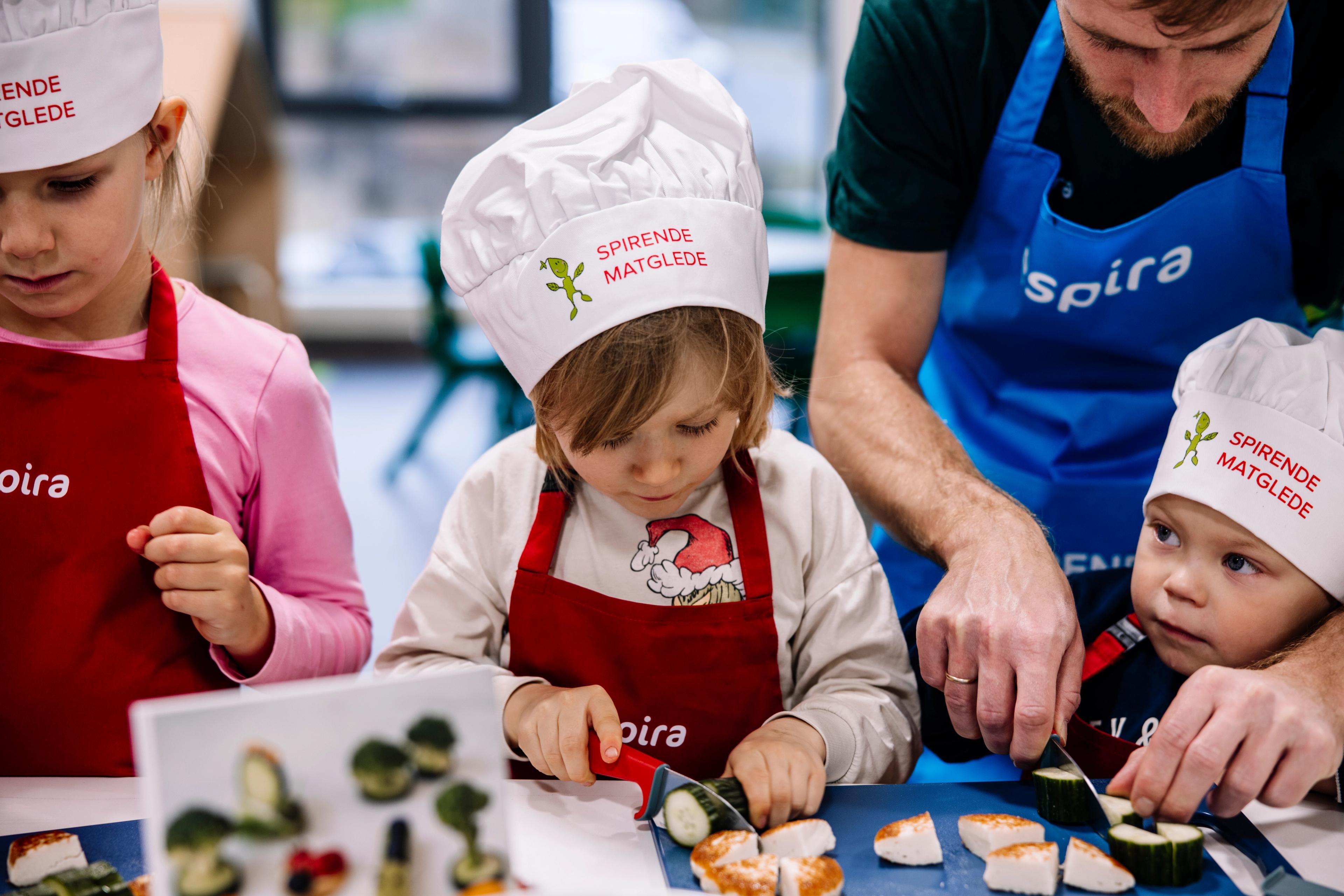 Tre barn får hjelp til å skære agurk og fiskekaker.