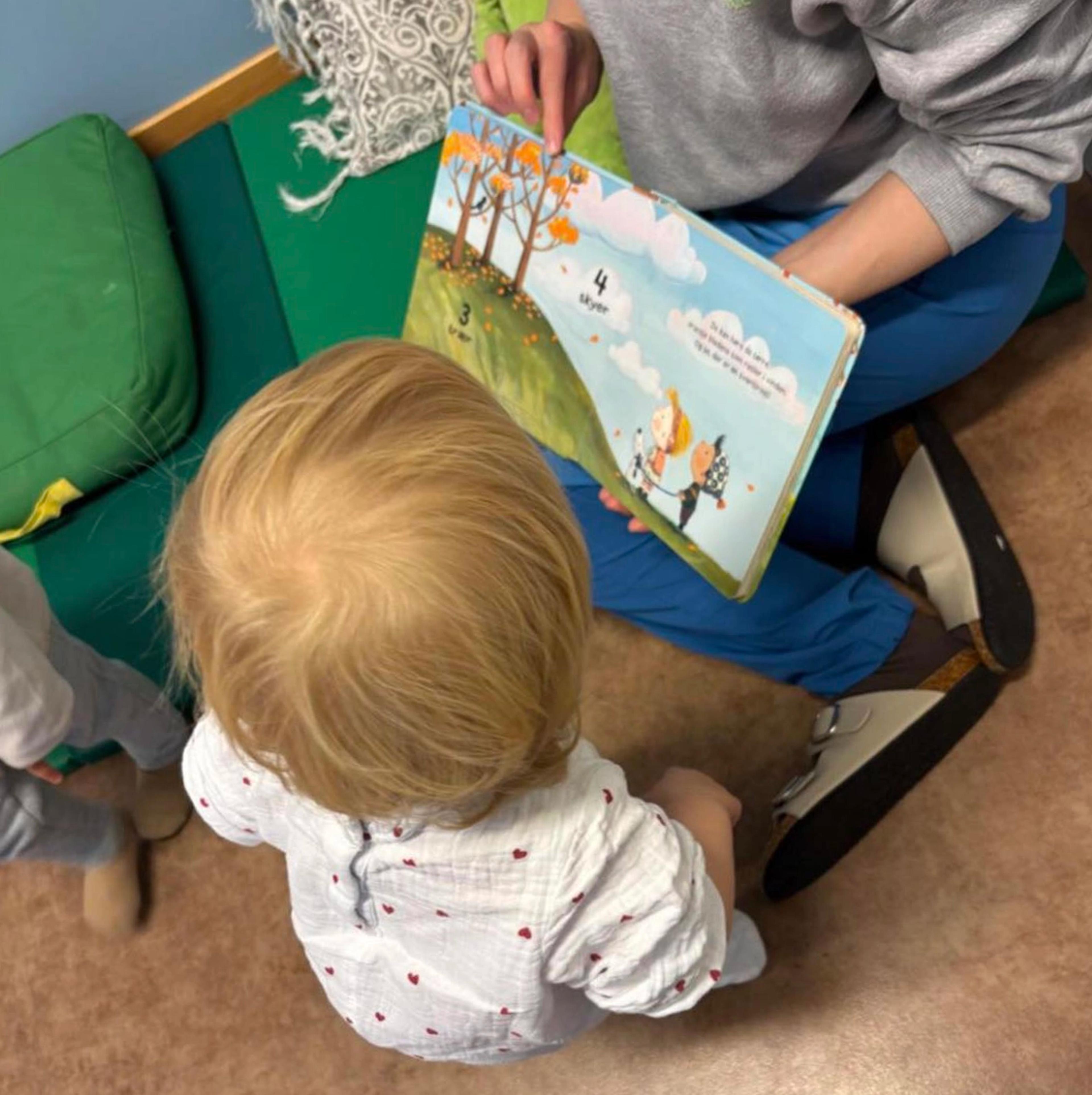 Ansatt som leser bok med barn i Espira Sandtoppen